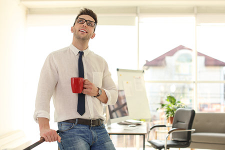Young businessman with cup of drink relaxing in office during breakの写真素材