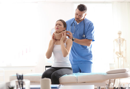 Male orthopedist applying cervical collar onto patient's neck in clinicの写真素材