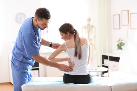 Male orthopedist examining patient's back in clinicの写真素材