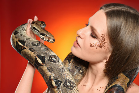 Beautiful woman with boa constrictor on bright colorful background, closeup