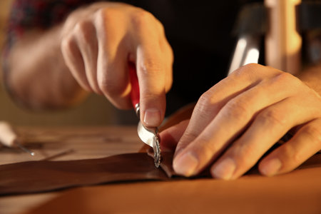 Man marking leather with roller in workshop, closeupの写真素材