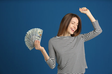 Happy young woman with cash money on blue backgroundの写真素材