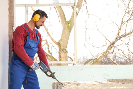 Worker using rotary drill hammer for window installation indoors