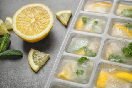 Ice cubes with lemon and mint in tray on gray table, closeupの写真素材