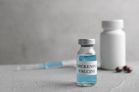 Chickenpox vaccine and syringe on gray table, space for text. Varicella virus prevention