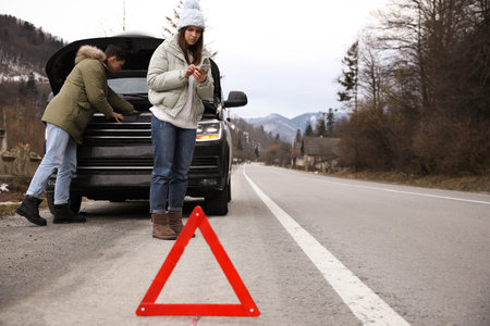 Stressed couple near broken car and emergency stop sign outdoors. winter day