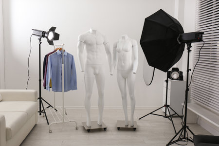 Ghost mannequins, clothes and professional lighting equipment in modern photo studio