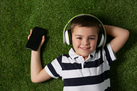 Cute little boy listening to audiobook on grass, top viewの写真素材
