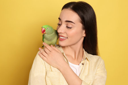 Young woman with Alexandrine parakeet on yellow background. cute pet