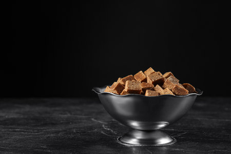 Metal bowl with brown sugar cubes on black table. Space for textの写真素材