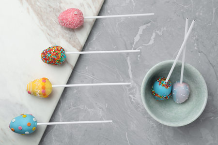 Egg shaped cake pops for Easter celebration on gray marble table, flat lay