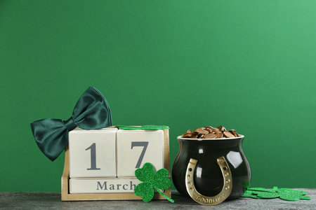 Composition with pot of gold coins and wooden block calendar on gray stone table against green...