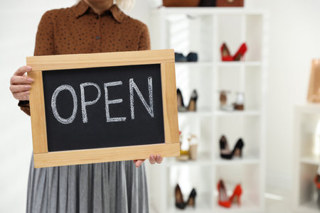 Female business owner holding OPEN sign in boutique, closeup. Space for text