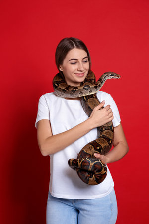 Young woman with boa constrictor on red background. exotic pet