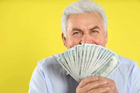 Emotional senior man with cash money on yellow backgroundの写真素材
