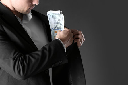 Man putting bribe money into pocket on black background, closeup. Space for text