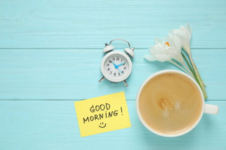 Delicious coffee, flowers and card with GOOD MORNING wish on light blue wooden table, flat lay. Space for textの写真素材