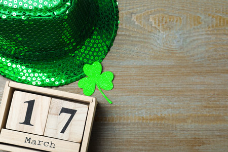 Green leprechaun hat, clover leaf and wooden block calendar on table, flat lay with space for text....