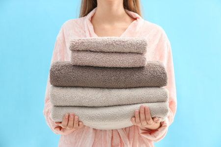 Woman holding stack of fresh clean towels on light blue background, closeupの写真素材