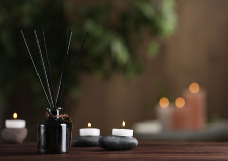 Reed air freshener, spa stones and burning candles on wooden table. Space for textの写真素材