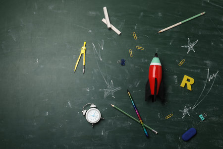 Bright toy rocket, school supplies and drawings on chalkboard, flat lay. Space for textの写真素材