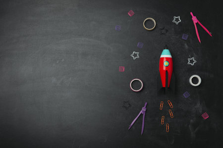 Bright toy rocket and school supplies on chalkboard, flat lay. Space for textの写真素材