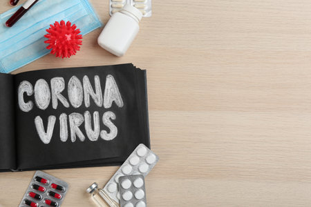 Notepad with words CORONA VIRUS and medicines on wooden background, flat lay. Space for textの写真素材