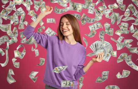 Happy young woman with dollars under money rain on pink backgroundの写真素材