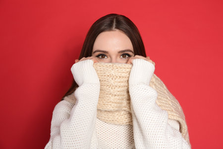 Young woman wearing warm sweater and scarf on red background. winter seasonの写真素材