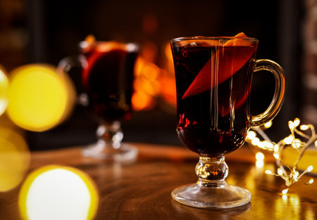 Tasty mulled wine, festive lights and blurred fireplace on backgroundの写真素材