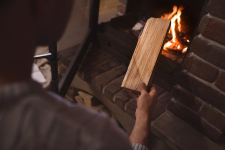 Man putting dry firewood into fireplace at home, closeup. winter holidays