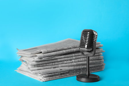 Newspapers and vintage microphone on light blue background. Journalist's workの写真素材