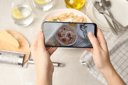 Food blogger taking picture of tasty pasta with shrimps and tomatoes at light table, closeupの写真素材