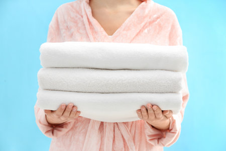 Woman holding stack of fresh clean towels on light blue background, closeupの写真素材