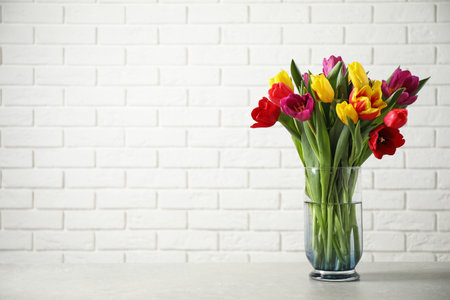 Beautiful spring tulips in vase on table near white brick wall. Space for textの写真素材