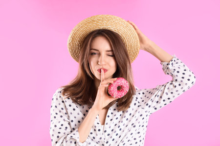 Beautiful young woman wearing stylish hat with donut on light pink backgroundの写真素材