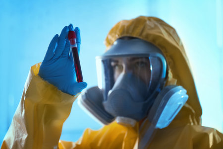 Scientist in chemical protective suit holding test tube with blood sample at laboratory, focus on hand. virus researchの写真素材
