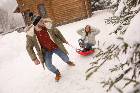 Young man pulling sled with his girlfriend outdoors on snowy day. winter holidaysの写真素材