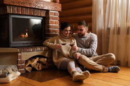 Lovely couple with glasses of wine near fireplace at home. winter holidaysの写真素材