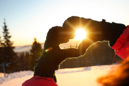 Woman making heart with hands outdoors at sunset, closeup. winter holidaysの写真素材