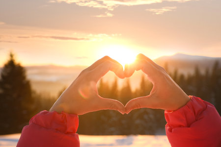 Woman making heart with hands outdoors at sunset, closeup. winter holidaysの写真素材