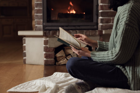 Woman reading book near burning fireplace at home, closeupの写真素材