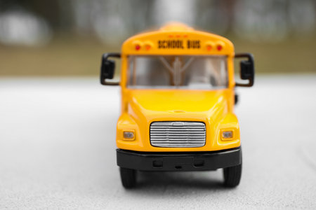 Yellow toy school bus against blurred background, closeup. Transport for students
