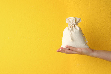 Woman holding full cotton eco bag on yellow background, closeup. Space for textの写真素材