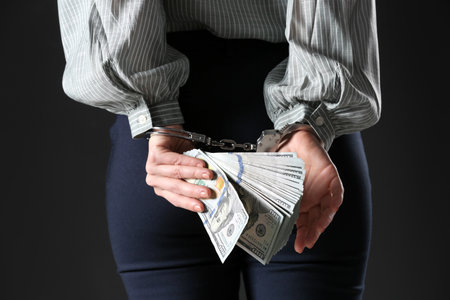 Woman in handcuffs holding bribe money on black background, closeupの写真素材
