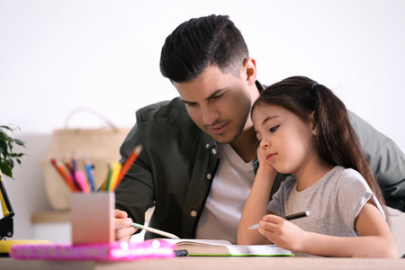 Man helping his daughter with homework at table indoorsの写真素材