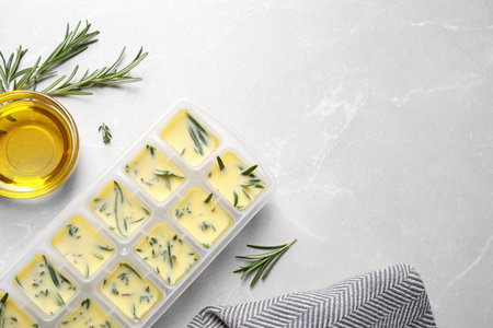 Ice cube tray with herbs frozen in oil and fresh rosemary on gray table, flat lay. Space for textの写真素材