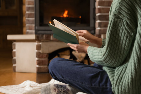 Woman reading book near burning fireplace at home, closeupの写真素材