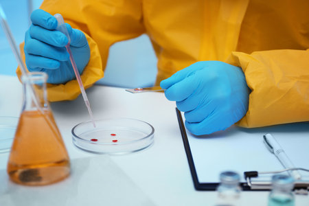 Scientist in chemical protective suit dripping reagent into Petri dish at laboratory, closeup. virus...