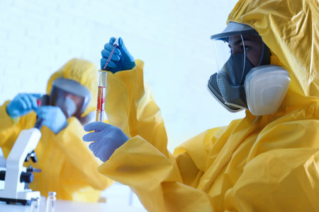 Scientist in chemical protective suit dripping blood into test tube at laboratory. virus research